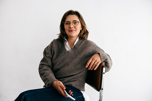 Portrait of a woman with smartphone as she sits casually on a chair in the studio