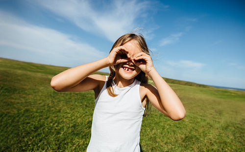 Girl pretending to use hand binoculars in sunny open field
