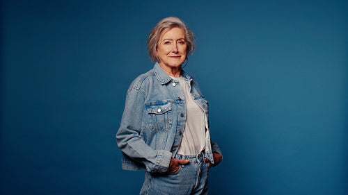 Confident senior woman smiling in denim on blue background