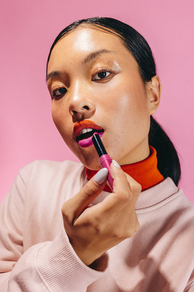 Going for a two-toned lip, young woman applies lipstick in a studio