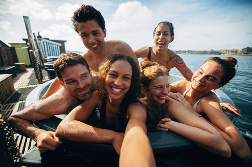 Group of friends takes a selfie with a phone in an outdoor hot tub during vacation.