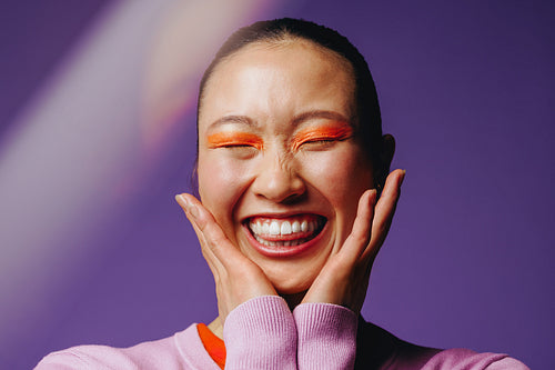 Asian woman with bold makeup smiling joyfully in a studio portrait