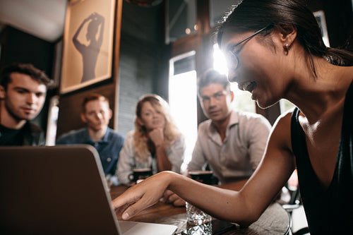 Young woman pointing at laptop and discussing with friends