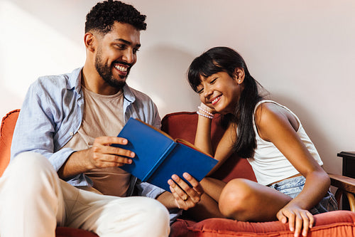 Father and daughter sharing a joyful moment while reading together on a couch