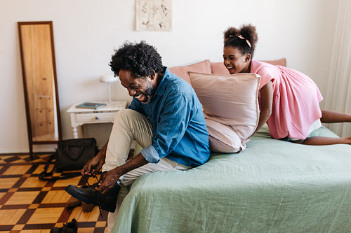 Happy daughter pillow fighting her dad while he gets ready for work