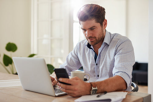 Young man working with laptop and mobile phone at his home office