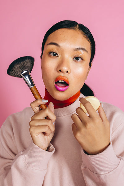 Asian woman in her 20’s doing her makeup using a makeup brush