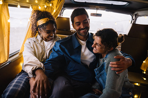 Three friends share a warm embrace inside a van with string lights