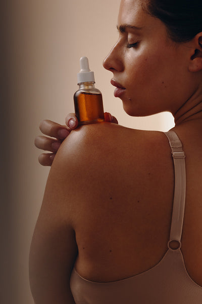 Woman holding facial oil bottle on her shoulder