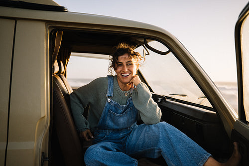 Woman smiles happily while sitting in a vintage van wearing denim overalls