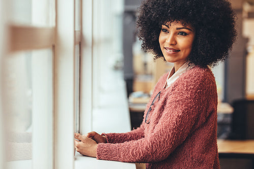 Portrait of a smiling woman standing beside a window