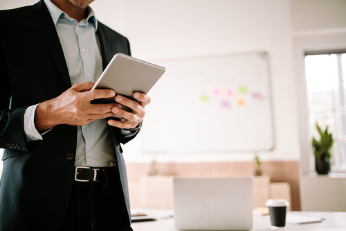 Businessman holding a digital tablet in hand standing in his office room