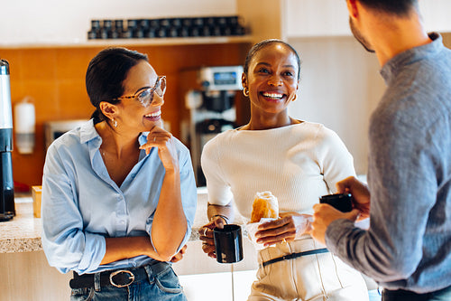 Group of coworkers chatting informally while enjoying coffee in the office kitchen