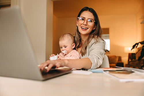 Happy single mom typing on a laptop in her home office