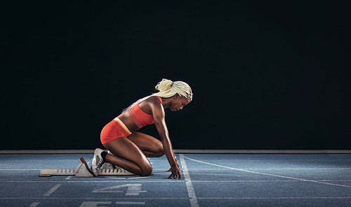 Woman sprinter using a starting block to start her sprint on a running track