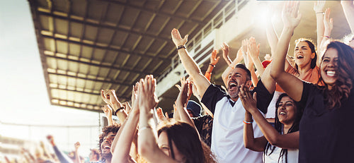 Crowd of sports fans cheering during a match in a stadium - people excited cheering for their favorite sports team to win the game