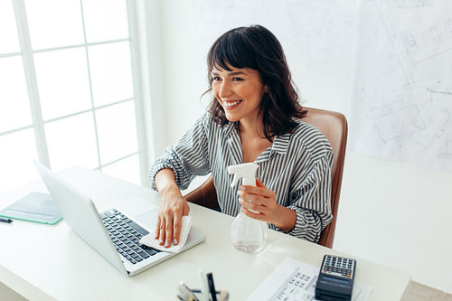 Businesswoman cleaning her laptop with sanitizer