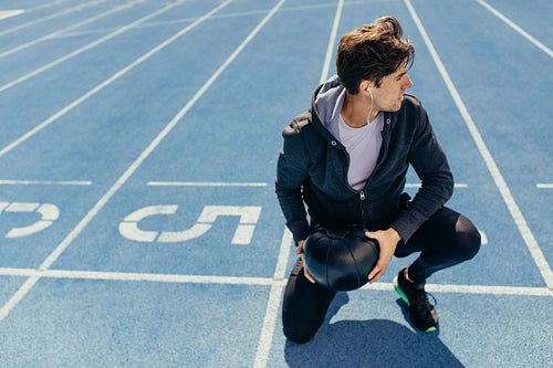 Athlete sitting on the running track with a medicine ball