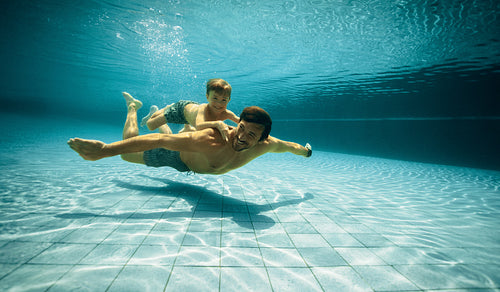Smiling father and son having fun underwater in swimming pool