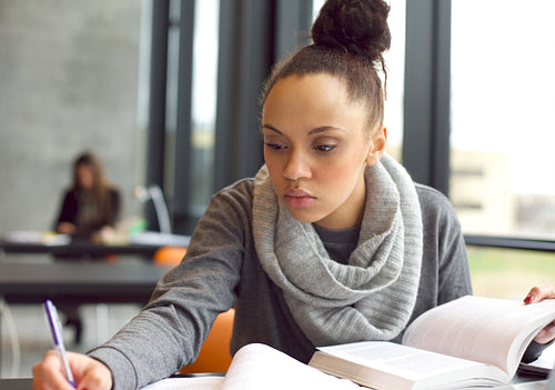 Young afro american woman doing assignments in library