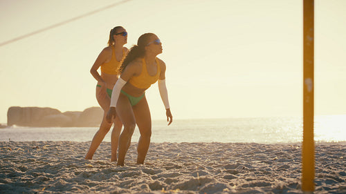 Professional female beach volleyball athletes lose intense rally at sunset