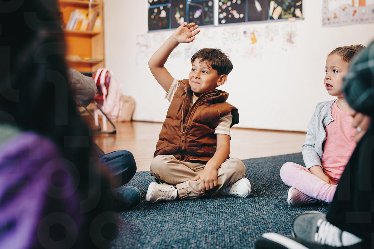 Smart elementary school kid raises his hand to give an answer in class ...
