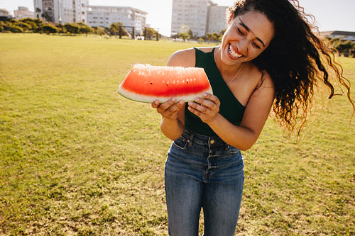 Smiling woman enjoying a juicy slice of watermelon on a sunny day in the city park, embracing summer lifestyle