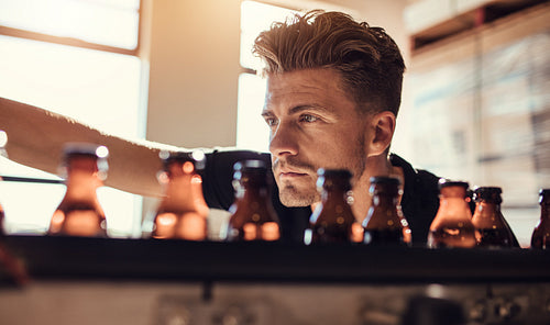 Man examining the beer bottles on conveyor at brewery factory