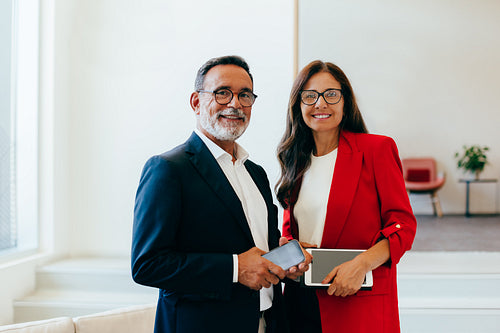 Smiling senior business professionals posing in formal attire holding tech devices