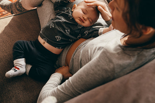 Mother sitting on couch with her baby sleeping on her