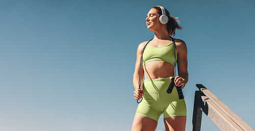 Female athlete in her 30s outdoors taking a break from her cardio workout, holding a skipping rope and wearing sportswear