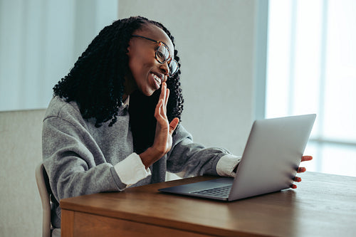 African woman happily waving during a video call, greeting someone on her laptop
