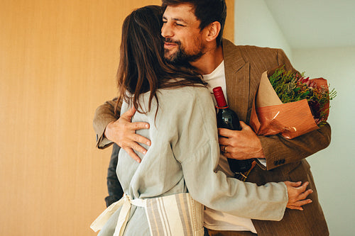 A cheerful man giving wine and flowers to a female host at dinner