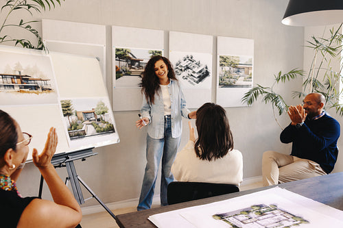 Young female architect presenting her design during a meeting with applause