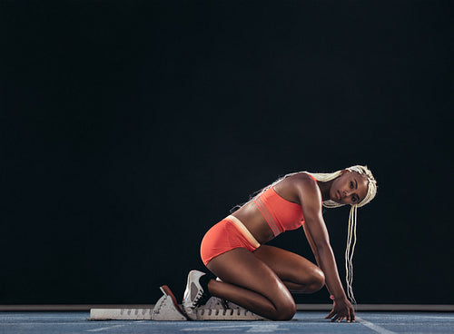 Female sprinter at the start line taking position on a running track