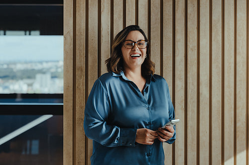 Smiling business woman stands with a smartphone in a modern office during communication