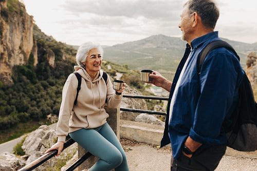 Cheerful senior couple taking a coffee break while hiking outdoo