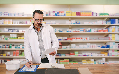 Male pharmacist writing prescription at workplace