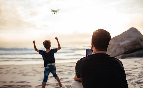 Father operating drone at beach and son cheering