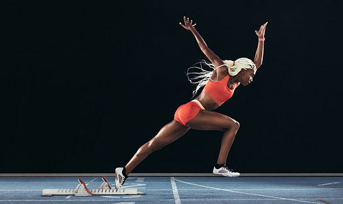 Woman athlete taking off from starting block on a running track