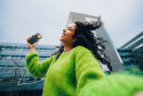 Young woman dancing to music with smartphone in urban setting