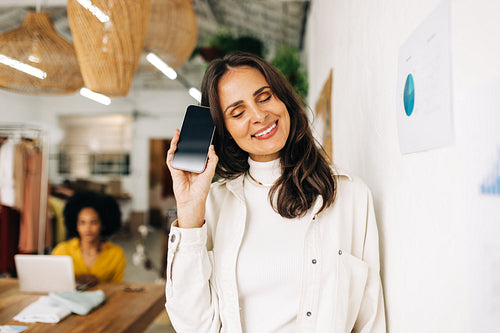 Technology for small business: Happy woman holding up a smartphone in a fashion store