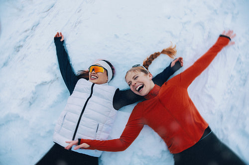 Women celebrate in the snow making winter angels after workout