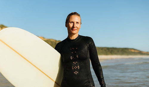 Mature female surfer posing with a surfboard on a sunny beach
