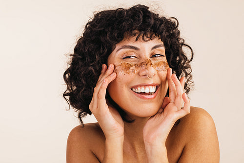 Happy young woman applying coffee scrub on her face