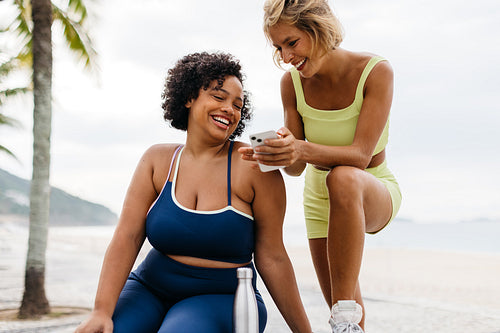 Two young women using a fitness app to monitor their progress after a beach workout
