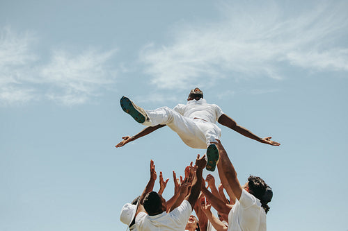 Cricket players celebrating by tossing a teammate cheerfully in the air outdoors