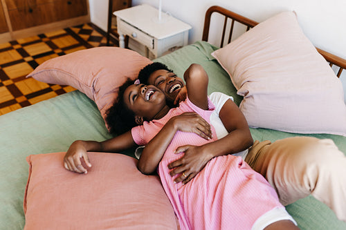 Playful mom cuddling her little daughter on the bed