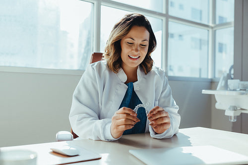 Female dentist examines aligner at modern office desk