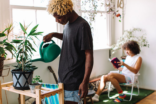 Young gay man watering a pot plant at home